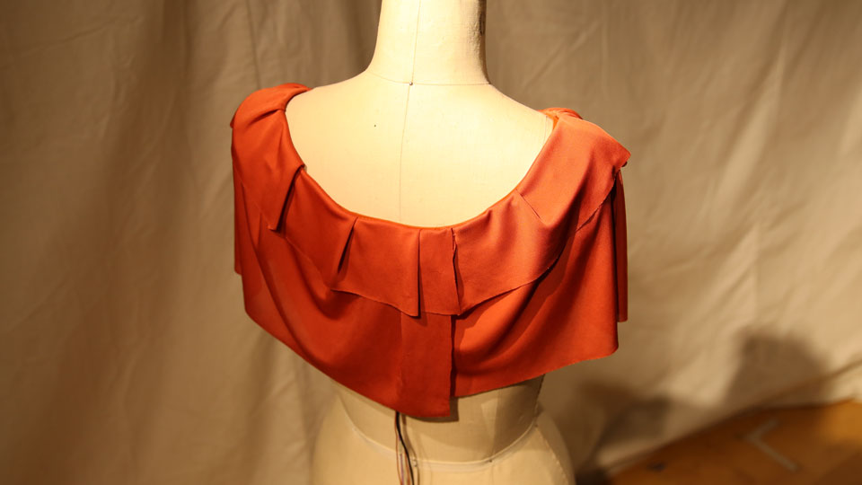 Photo of the back of the wearable piece. The orange ruffled shirt neck is placed on a manequin. There are wires coming down from the back of the fabric.