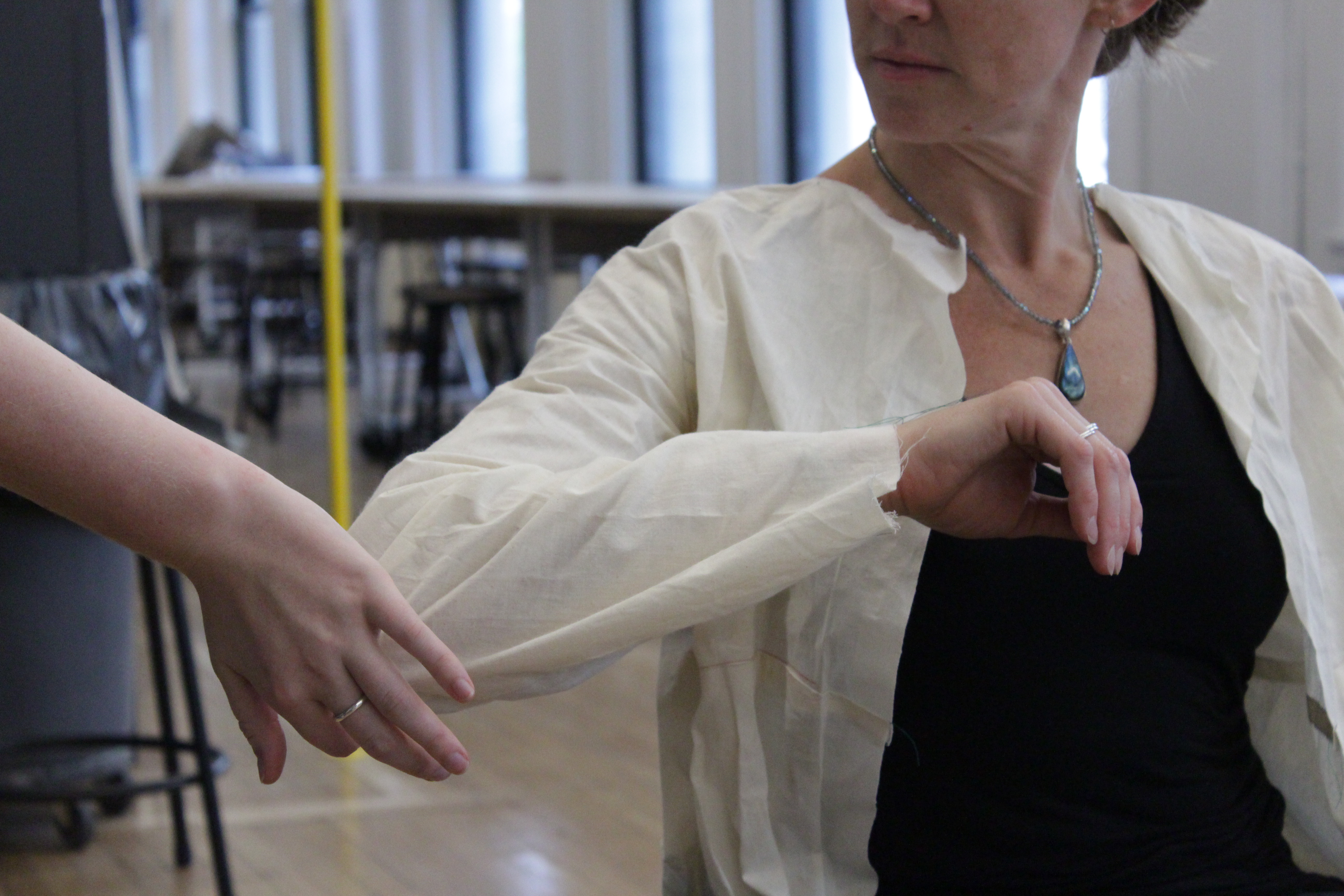 Photo of April trying a pattern prototype of the jacket. She is flexing her right elbow and there is a hand touching her elbow.
