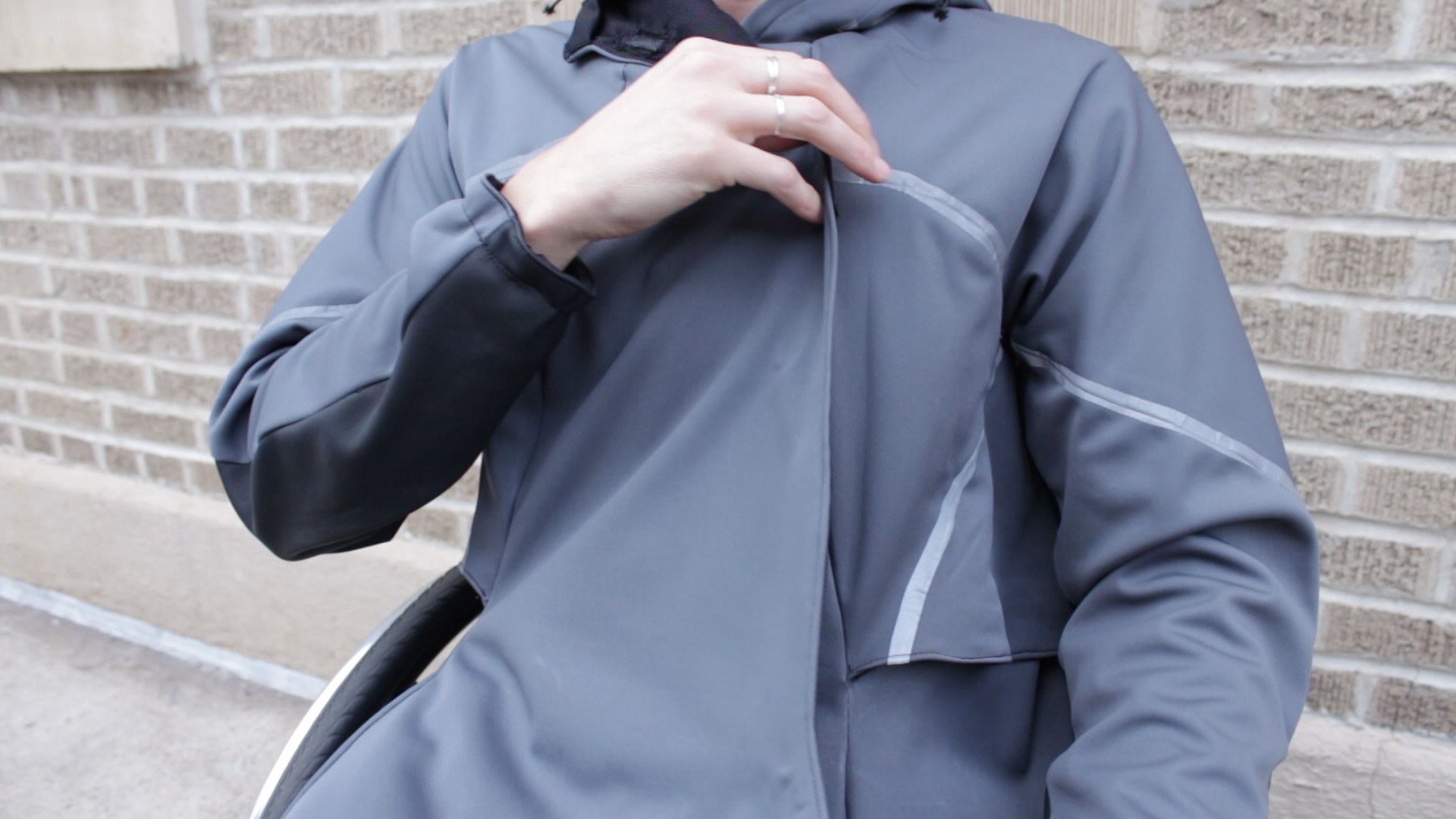 Photo of April closing the jacket. The jacket is grey, the seams have a grey reflective fabric and the back part of the sleeves is made of black leather.