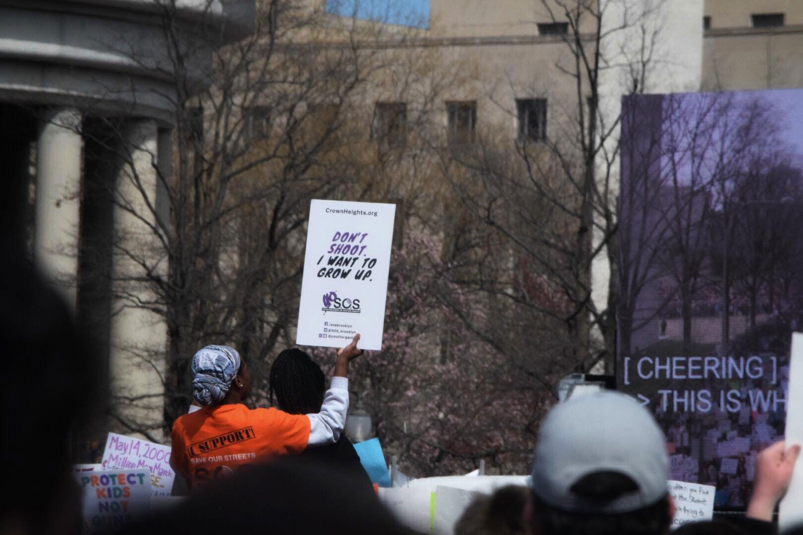 Photo showing a student of color in a crowd holding a poster that has the following written on it: Don't shoot. I want to grow up.