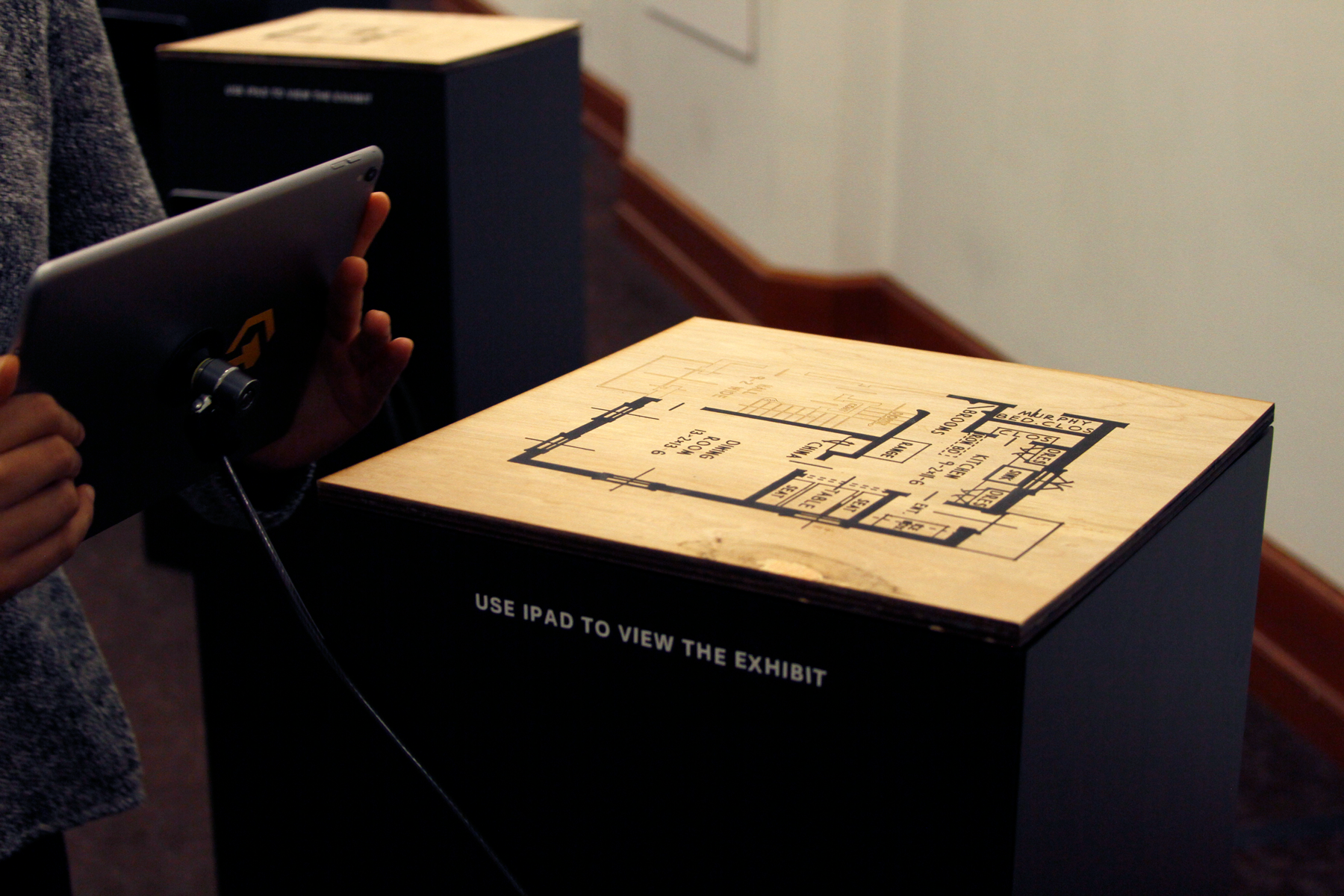 Photo showing a scaled floor plan on a wooden surface, on top of a black plinth. They served as the visual tag to activate the augmented reality experience.