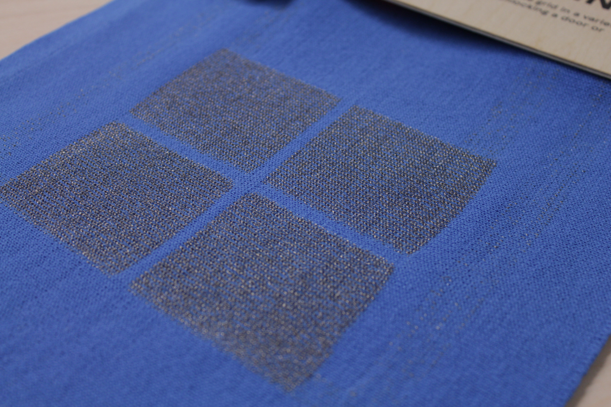 Photo of the knitted fabric. The fabric is blue and in the middle there are four grey squares knitted with conductive thread.