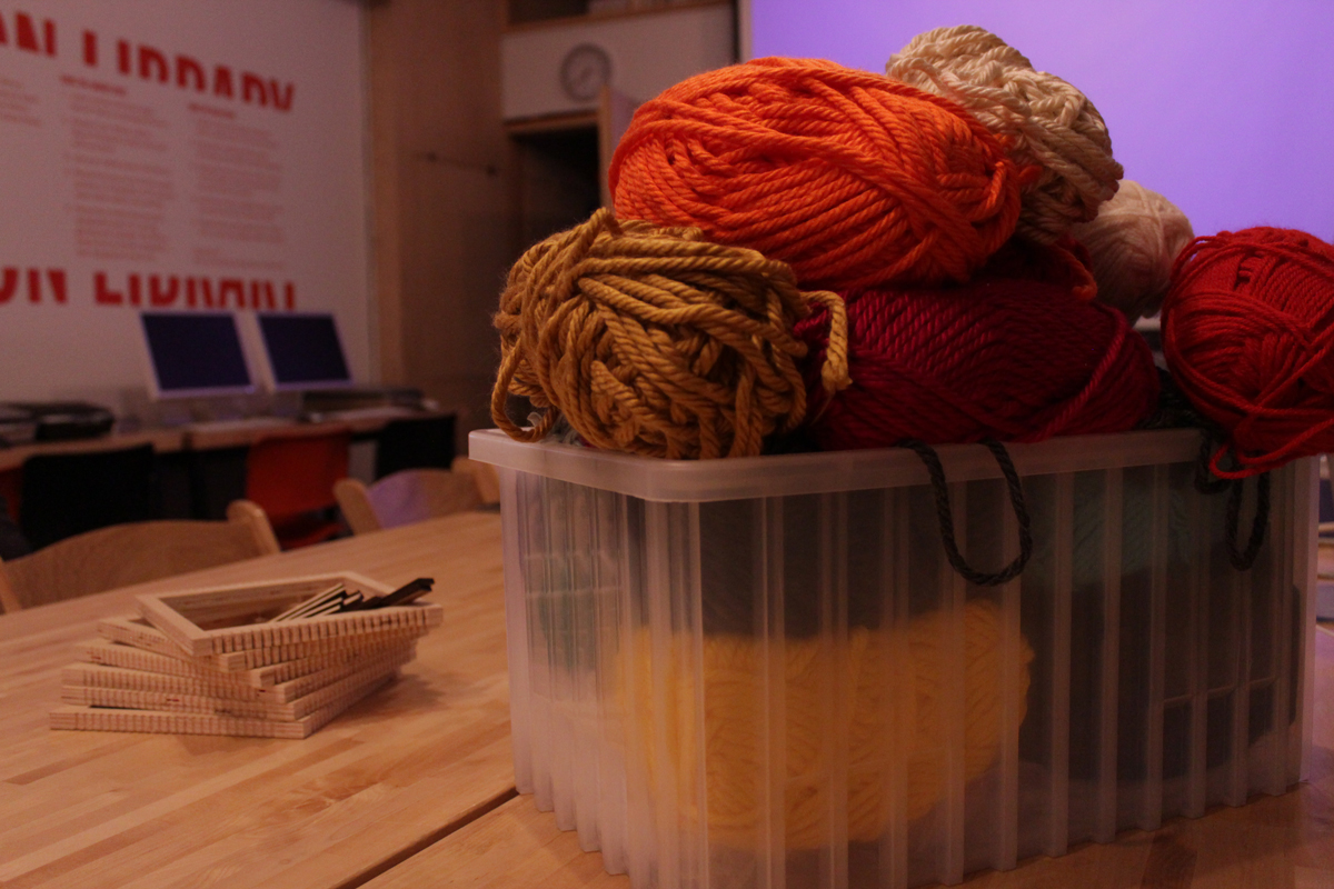 Photo of a box full with different color yarns. On the left there are small wooden weaving frame looms.